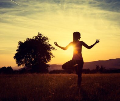 Young athletic woman practicing yoga on a meadow at sunset, silhouette